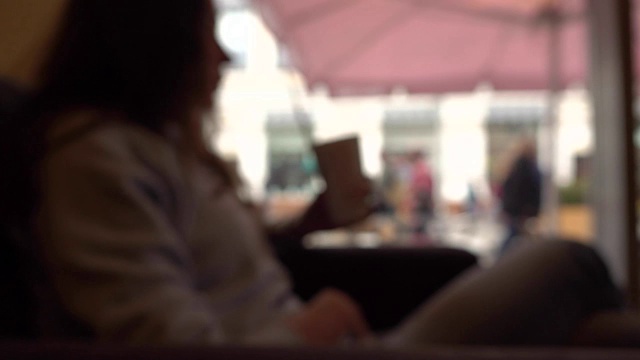 模糊的黑发女孩有她的饮料与吸管在一个咖啡馆靠窗。慢动作背景散景拍摄
