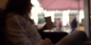 模糊的黑发女孩有她的饮料与吸管在一个咖啡馆靠窗。慢动作背景散景拍摄