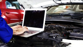 女机械师在维修汽车引擎时使用笔记本电脑视频素材模板下载