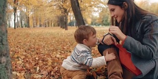 在秋天的公园里，小男孩看着妈妈手上的钟表