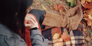 美丽、时尚、年轻的女性在秋天的公园里坐在格子上使用智能时钟。FullHD