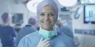 手术室手术成功后，积极、迷人、微笑的护士摘下手术口罩肖像。