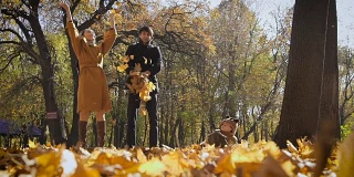 快乐的一家人在公园里玩着秋叶。妈妈和爸爸向空中抛了一圈链子。小孩子看着他们玩得很开心