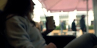 散焦的黑发女孩坐在窗前，用吸管在咖啡馆喝她的饮料。全高清背景散景剪辑