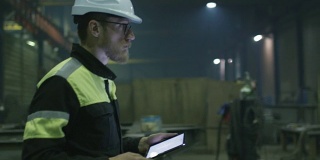 戴安全帽的工程师正带着一台平板电脑穿过一家重工业工厂。