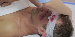 护士用绷带包扎头部。一个脸上有淤青的受伤男子