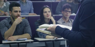一位大学教授正在给一个多民族学生上课，他手里拿着一本书。