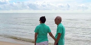 一对亚洲老年夫妇在海滩上愉快地散步。手牵着手，互相交谈