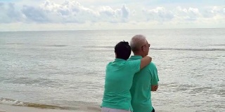 一对亚洲老年夫妇在海滩上愉快地散步。手牵着手，互相交谈