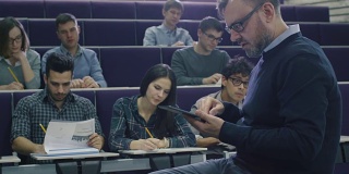 一位大学教授正在给一群来自不同民族的学生上课，他正在检查一台平板电脑。