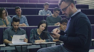 一位大学教授正在给一群来自不同民族的学生上课，他正在检查一台平板电脑。视频素材模板下载