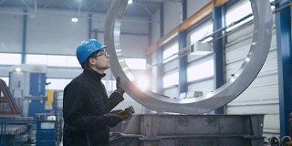 一名戴着安全帽的工人正在用远程起重机移动一个金属零件。
