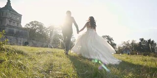 在日落城堡附近的草地上奔跑的新婚夫妇