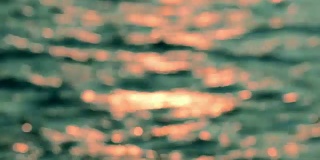 散焦镜头的波浪形水面与美丽的散焦太阳眩光，从水面反射