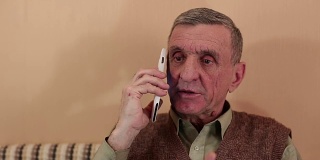 一位手持白色智能手机的老人会说话、微笑、打手势
