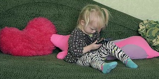 多莉小女孩坐在家里的沙发上和智能手机