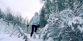 苗条的年轻女子穿着灰色的夹克走在美丽的雪地里，慢镜头拍摄，冷色