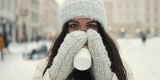 快乐，寒假，圣诞节，饮料和人的概念-微笑的年轻女子在白色温暖的衣服和喝咖啡带走了雪城的背景