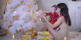 小婴儿和妈妈在圣诞树旁玩耍。新年装饰和概念的第一步