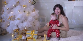 小婴儿和妈妈在圣诞树旁玩耍。新年装饰和概念的第一步