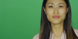 美丽的亚洲女人微笑，在一个绿色屏幕的工作室背景