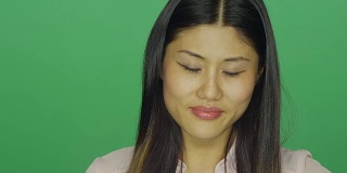 美丽的亚洲女人微笑和咯咯笑，在一个绿色屏幕的工作室背景