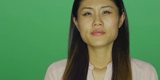 美丽的亚洲女人凝视前方，然后微笑，在一个绿色屏幕的工作室背景