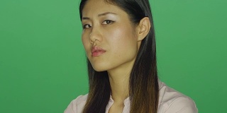 美丽的亚洲女人看起来失望与她的双臂交叉，在一个绿色屏幕的工作室背景