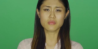 美丽的亚洲女人看起来悲伤，在一个绿色屏幕的工作室背景