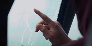 一个人用一根手指在车窗上画画。外面下雨的天气。滴