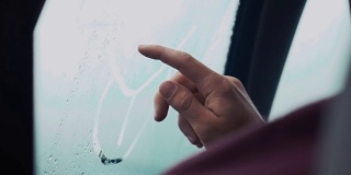 一名男子用一根手指在车窗上画画。外面下雨的天气。滴