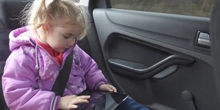 小女孩暖和衣服，在车上玩平板电脑