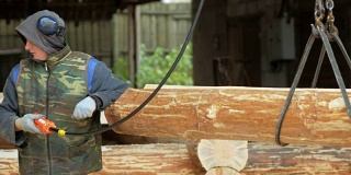 建筑工用吊车吊起木材。一个男人拿着一根木头，把它搬到未来的家