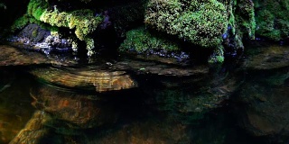 瀑布飞溅的慢镜头近景，泉水下落时，滴落在覆盖着绿色苔藓的岩石上