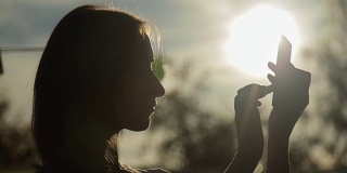 日落时拿着智能手机的女人的剪影