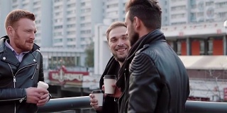 三个留着胡子的英俊青年在城市的一座桥栏杆附近聊天，边喝咖啡边聊天。缓慢的莫
