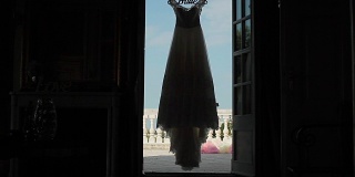 婚纱挂在门口的背光剪影。黑色魅影婚纱配以天台或阳台为背景的新娘礼服专用吊架上