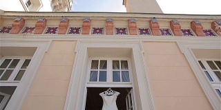 婚纱挂在阳台的跟踪盘上，在门口垂直发光。装饰蕾丝白色新娘礼服衣架等待新娘在中世纪古代阳台装饰元素。早上新娘准备