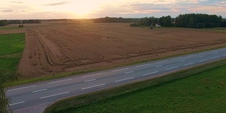 跟踪和航拍一辆卡车在高速公路上行驶。美丽的田野风景和夕阳被看到。