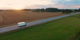 跟踪和航拍一辆卡车在高速公路上行驶。美丽的田野风景和夕阳被看到。