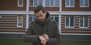 四合院。一个身穿灰色外套的男人走在路上，手里拿着一个钟，手指上戴着一枚戒指。他改变你手表上的设置，因为他做得很好而高兴