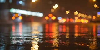 五颜六色的交通灯在水中倒映，夜晚的城市街道上有小雨滴。慢动作视频