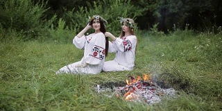 仲夏。两个穿着斯拉夫服装的女孩在火炉旁编着辫子。