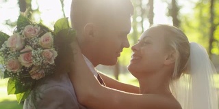 年轻的新娘和新郎在一个阳光灿烂的公园里接吻。