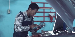 一个非洲机械师站在看一个汽车引擎