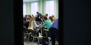 一大群人坐在一个明亮的教室里一起工作。年轻的经济学家坐在桌旁讨论实践，等待讲座的开始