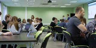 现代大学的教育过程。学生们分组坐在桌子旁，通过笔记本屏幕学习课程材料。宽敞的教室