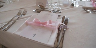 节日餐桌上的装饰布置紧凑——菜单和餐巾用粉色丝带系好。特殊场合的婚宴、周年纪念招待会或豪华餐厅的生日午餐餐具