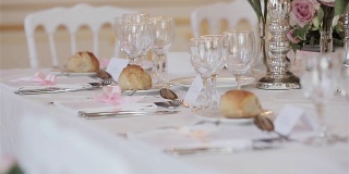餐具装饰布置的节日餐桌近距离变化，货架焦点细节。婚礼接待桌上的客人位卡，玻璃，餐具，鲜花和面包面包在盘子准备好