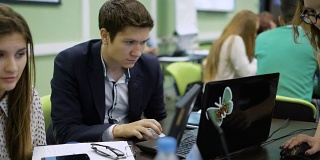 学生在实际经济任务中，用笔记本电脑工作。年轻人盯着屏幕。在前台，传送一部智能手机